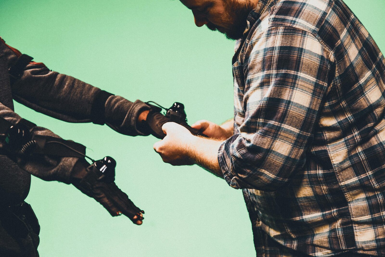 Crew member fitting a motion capture suit on an actor in front of a green screen on set