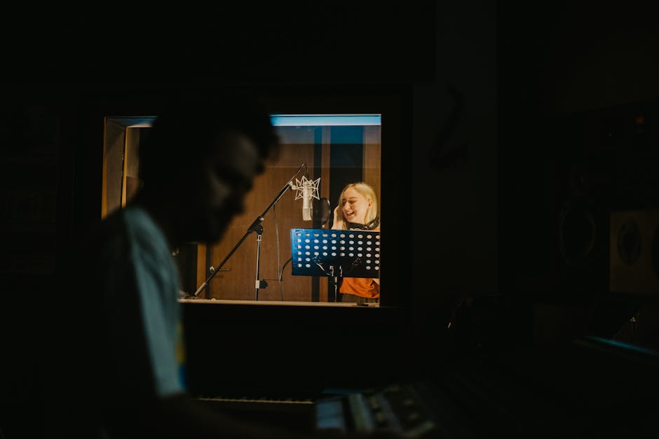 Actor recording dialogue at a condenser microphone in a dimly lit vocal booth, with script stand and studio glass visible