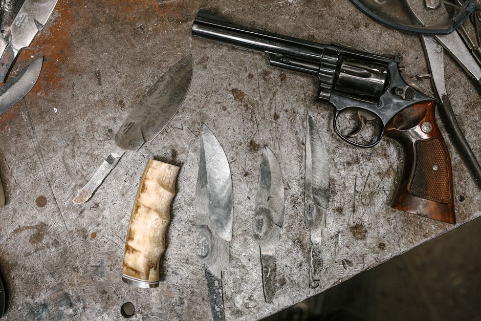 Assorted prop weapons laid out on a workshop table — a large revolver flanked by a collection of knives and blades of various sizes