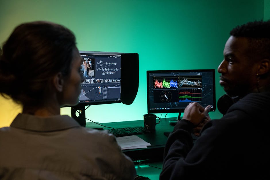 Editor and assistant editor collaborating at dual monitors in a professional editing suite, reviewing footage for a color grade session