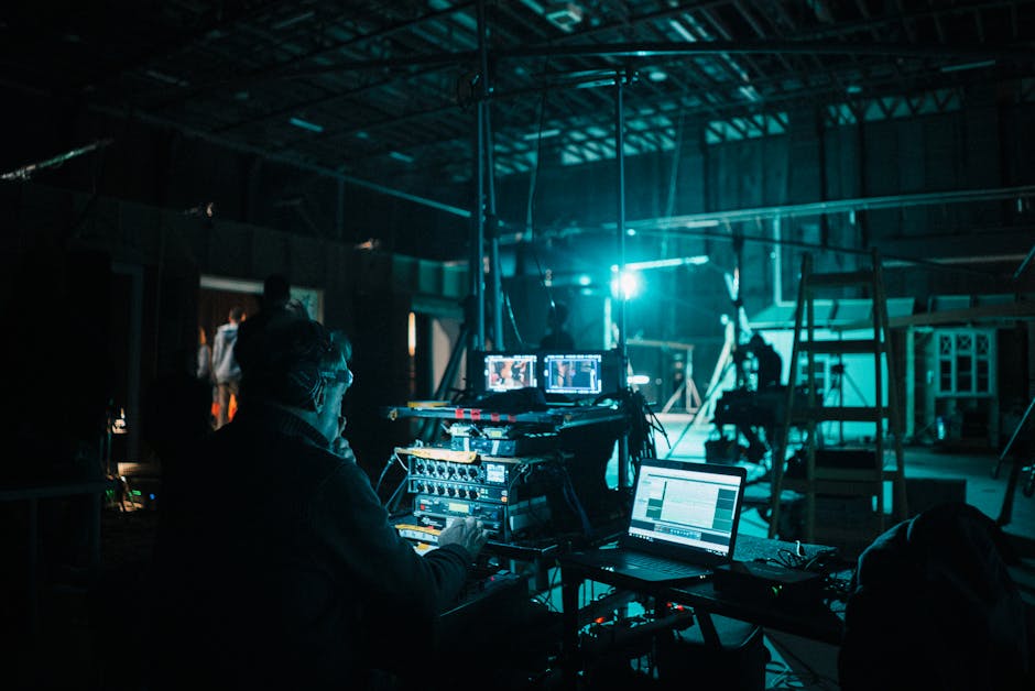 Behind the scenes on a dimly lit film set with a crew member monitoring multiple screens at the video village