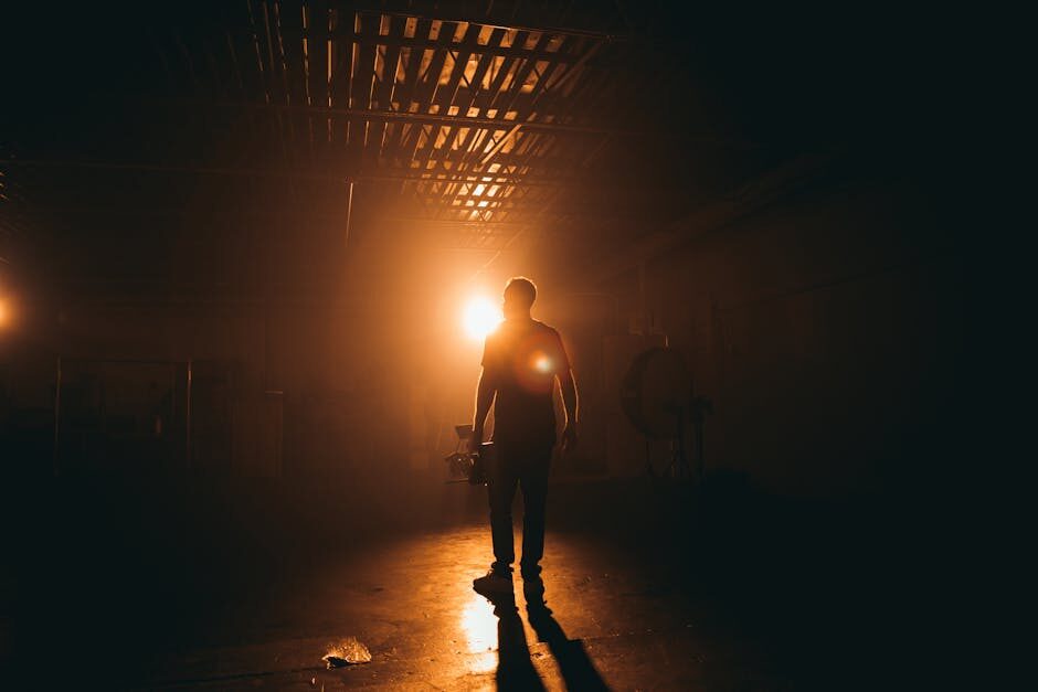 Crew member silhouetted against a tungsten backlight on a dark film set sound stage