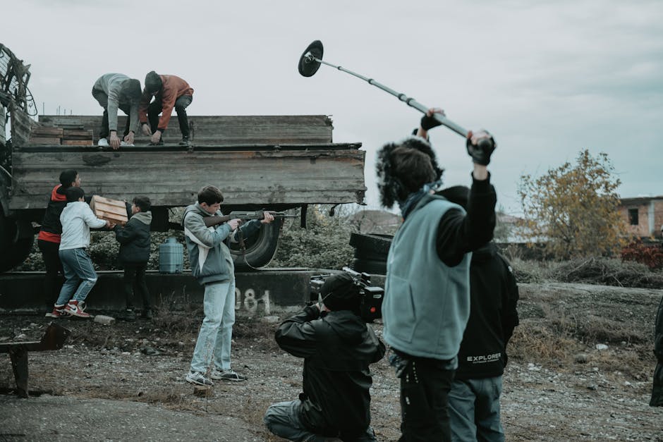 Boom operator holding a boom pole overhead during an active outdoor film shoot with camera crew