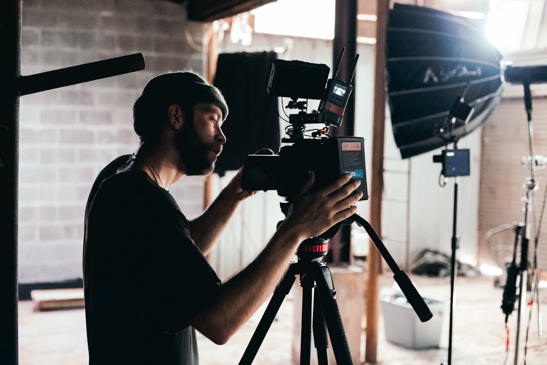 Camera operator adjusting a cinema camera on a tripod with professional lighting on a film set