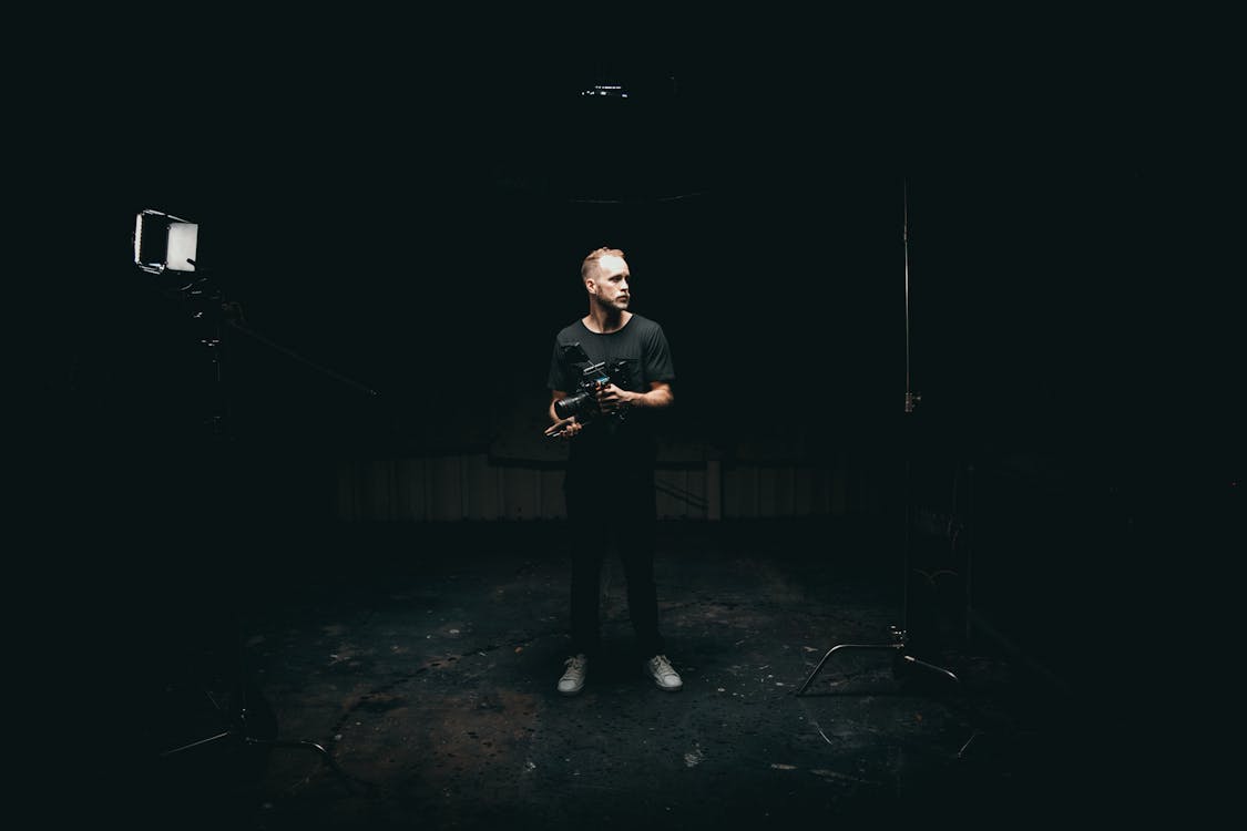 Cinematographer holding a cinema camera on a dark sound stage with a single light panel