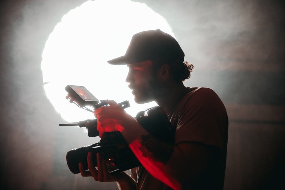 Silhouette of a cinematographer operating a camera handheld, backlit by a large soft light in a smoky atmosphere