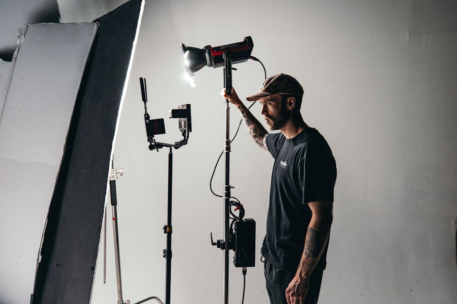 Lighting technician adjusting a film LED fixture on a C-stand during a studio shoot