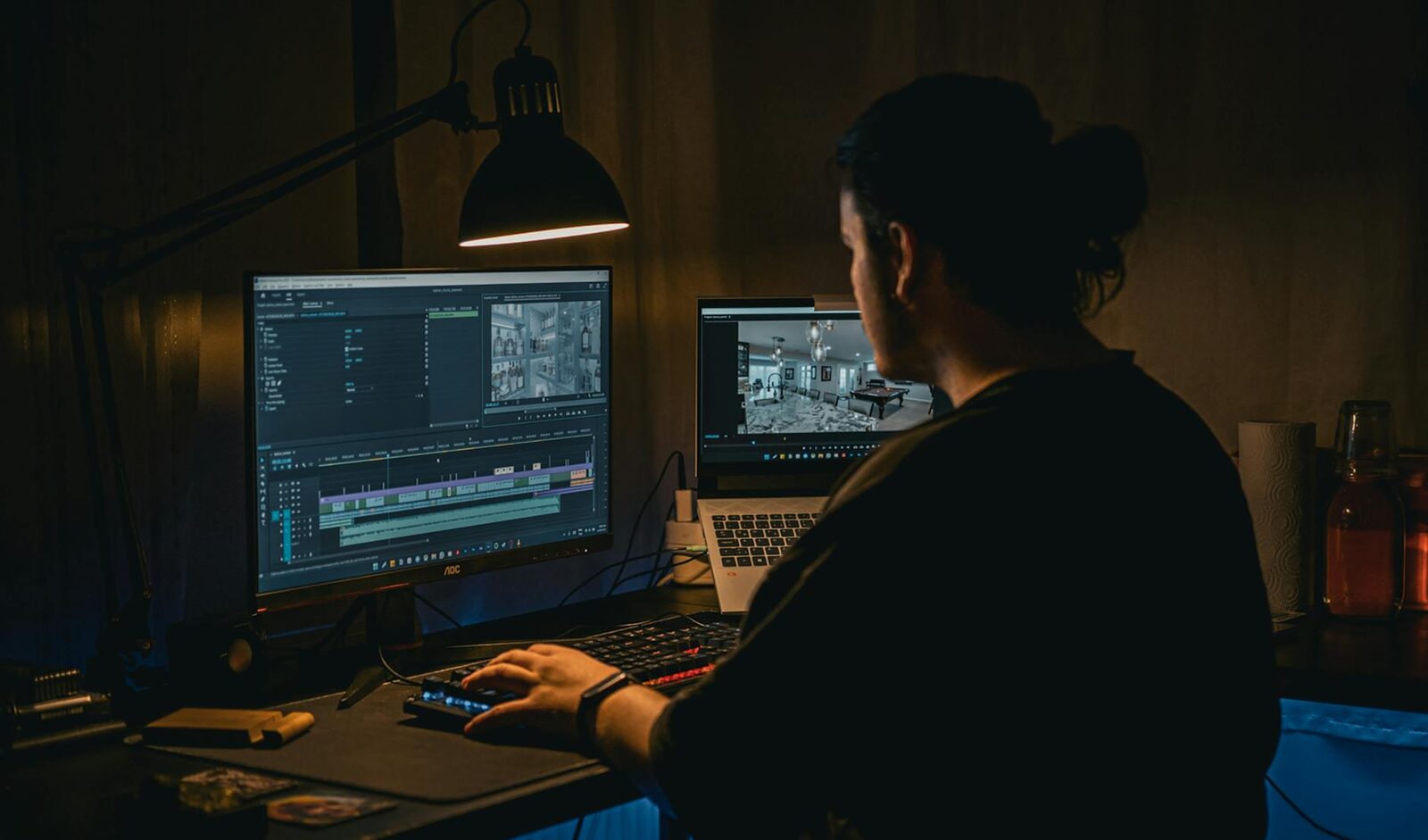 A film editor reviews footage and schedules in a dimly lit production workspace with dual monitors