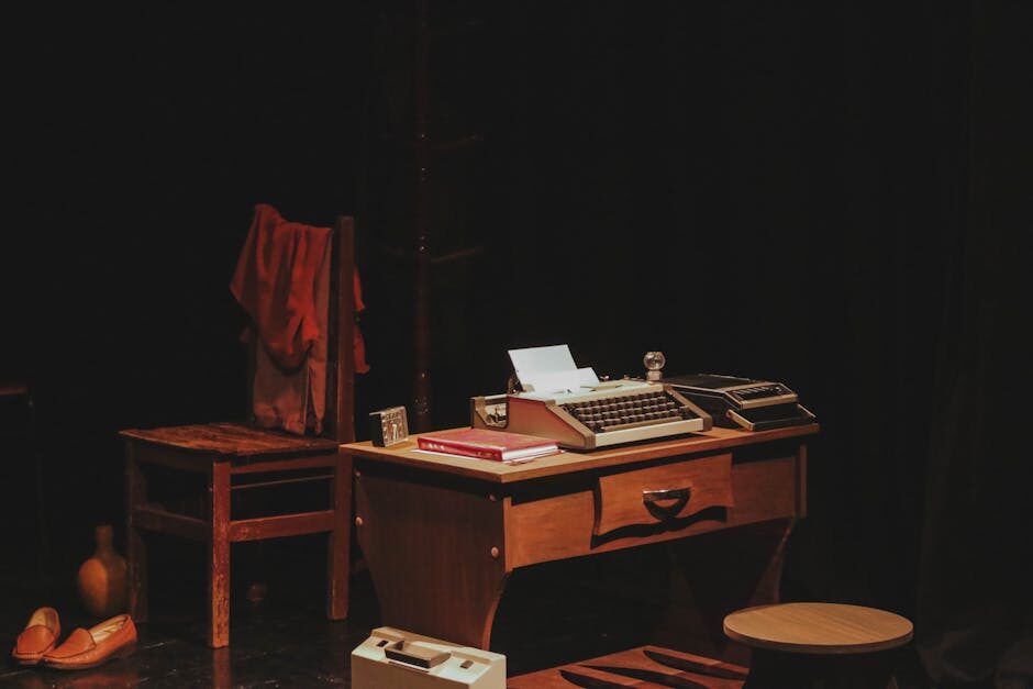 A fully dressed film stage set featuring a vintage wooden desk with typewriter, period props, and dramatic dark stage lighting