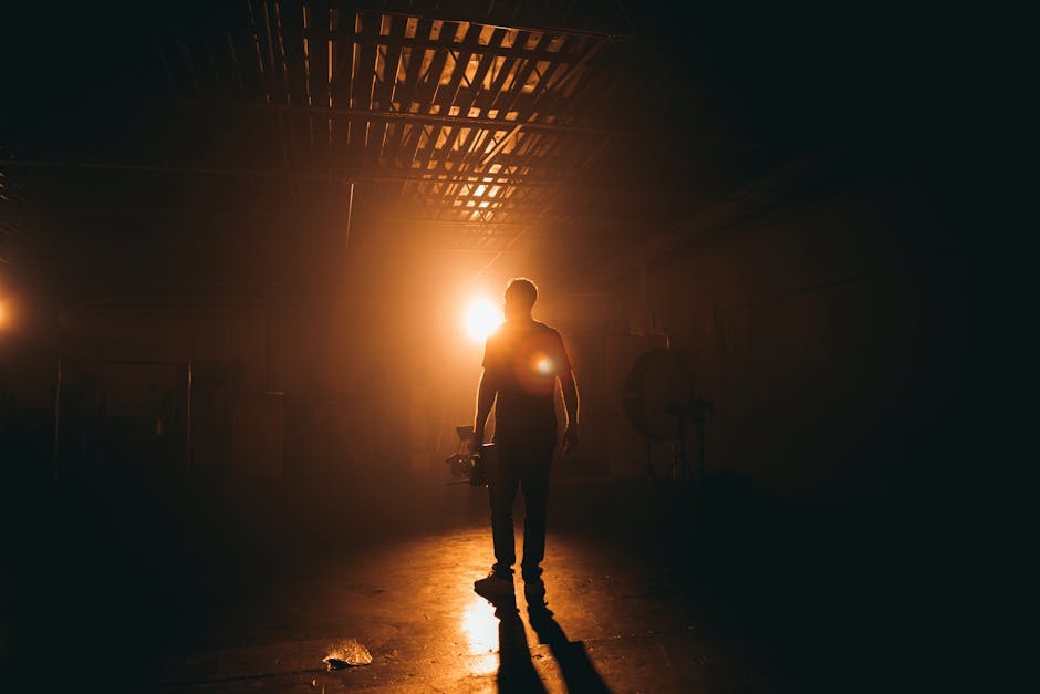 Silhouette of a cinematographer carrying equipment on a hazy, warmly lit film set warehouse